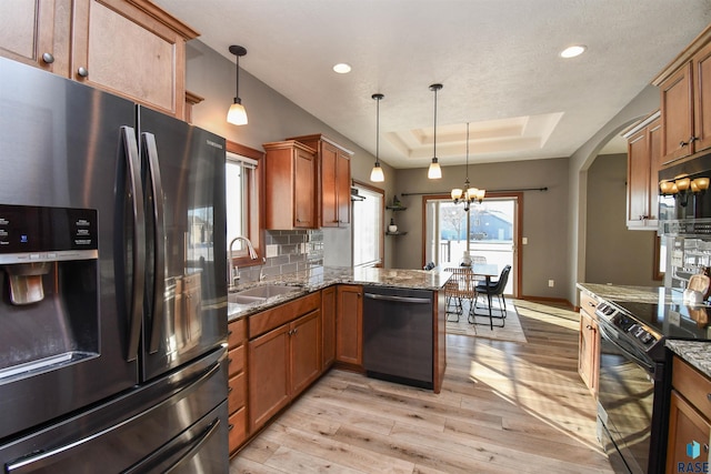 kitchen with black appliances, kitchen peninsula, hanging light fixtures, and a tray ceiling