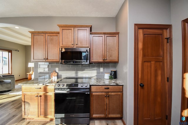 kitchen featuring tasteful backsplash, light stone countertops, light hardwood / wood-style flooring, and stainless steel appliances