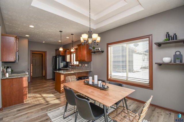 dining area featuring an inviting chandelier, light hardwood / wood-style floors, sink, and a tray ceiling