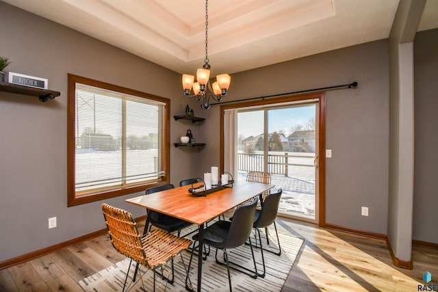 dining space with a raised ceiling, light hardwood / wood-style flooring, and an inviting chandelier