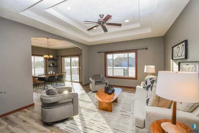 living room with ceiling fan with notable chandelier, light wood-type flooring, and a raised ceiling