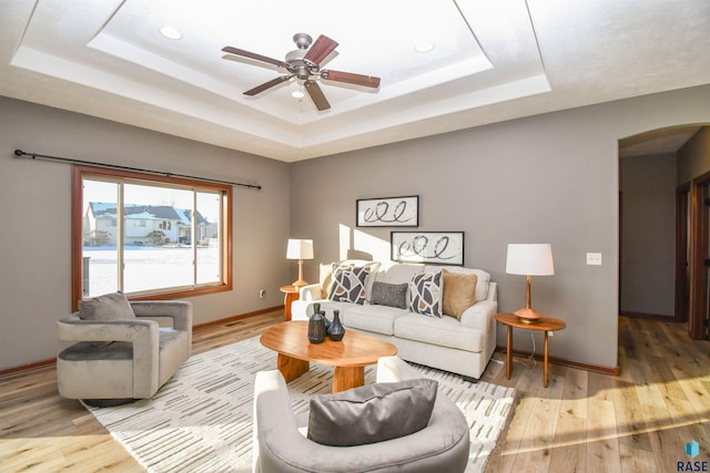 living room with ceiling fan, light wood-type flooring, and a tray ceiling