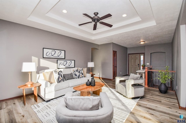 living room featuring light hardwood / wood-style flooring, a raised ceiling, and ceiling fan