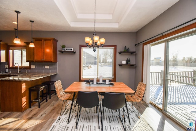 dining space with plenty of natural light, light wood-type flooring, a tray ceiling, and a chandelier