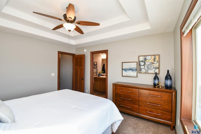 carpeted bedroom with a tray ceiling, connected bathroom, and ceiling fan