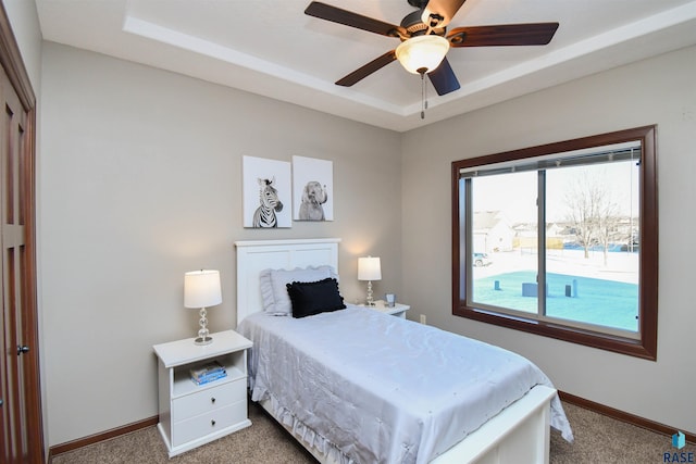 bedroom with ceiling fan, light carpet, and a tray ceiling