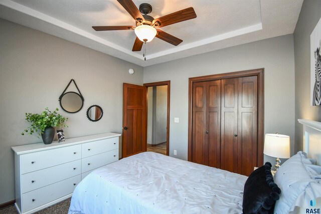 bedroom with ceiling fan, a closet, and a tray ceiling