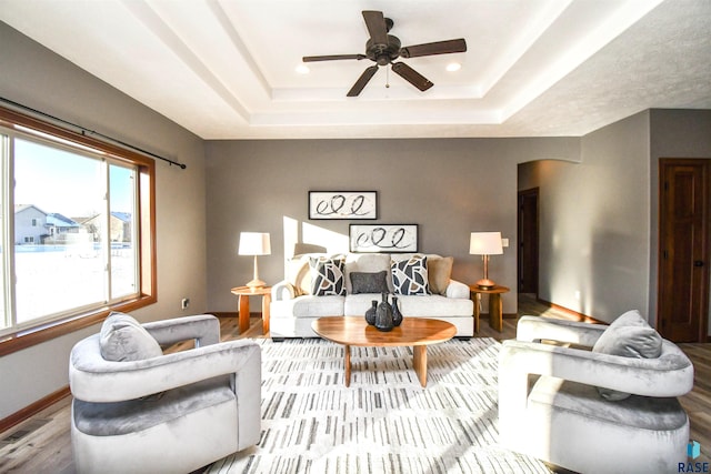 living room featuring ceiling fan, a raised ceiling, and light hardwood / wood-style flooring