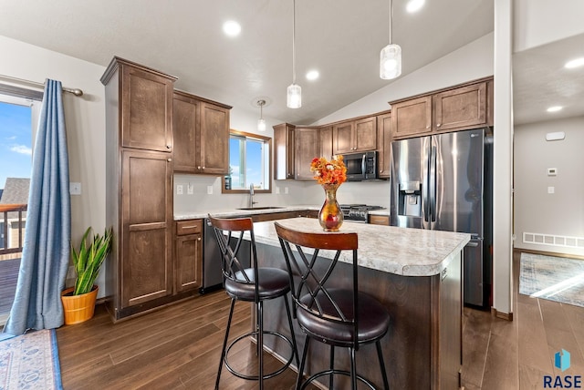 kitchen featuring dark wood-type flooring, a center island, hanging light fixtures, lofted ceiling, and appliances with stainless steel finishes