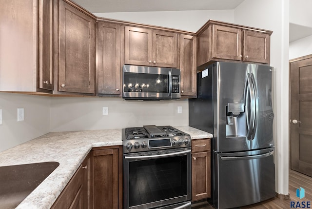 kitchen with stainless steel appliances, sink, vaulted ceiling, light stone counters, and hardwood / wood-style floors