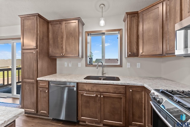 kitchen featuring light stone counters, dark hardwood / wood-style floors, hanging light fixtures, appliances with stainless steel finishes, and sink