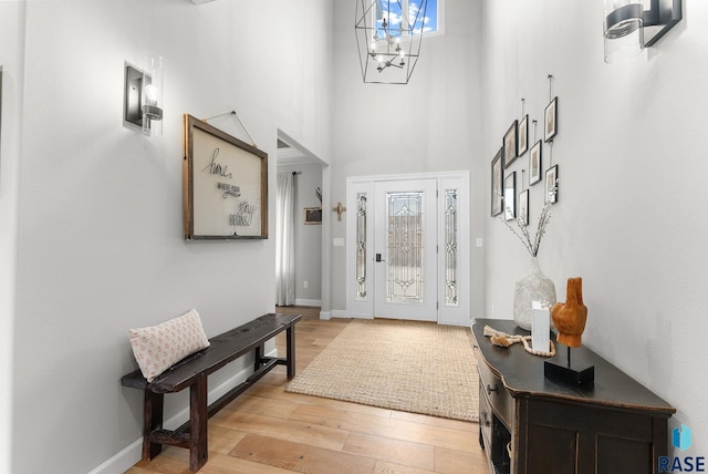 entryway with a towering ceiling, light wood-type flooring, and a chandelier