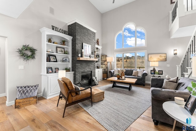 living room featuring a high ceiling, a brick fireplace, and light hardwood / wood-style flooring