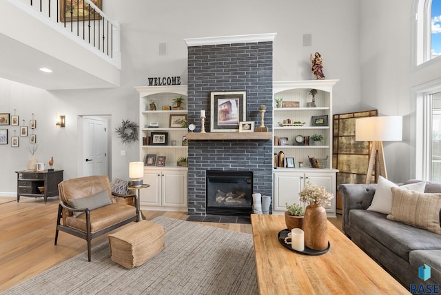 living room with light wood-type flooring, a towering ceiling, and a fireplace