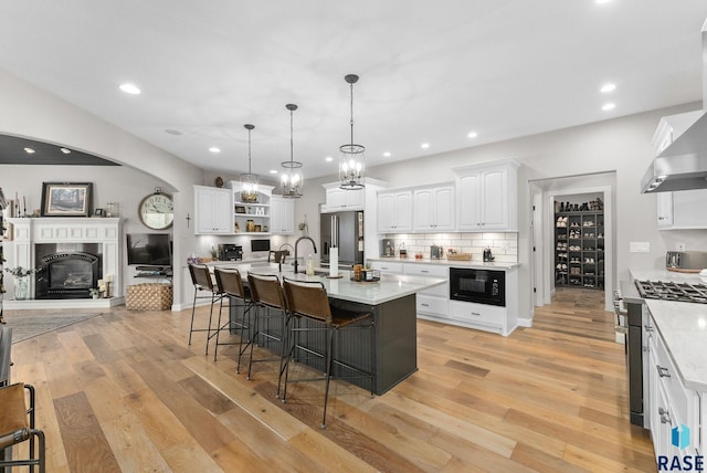 kitchen featuring light stone counters, hanging light fixtures, premium appliances, a kitchen island with sink, and white cabinetry