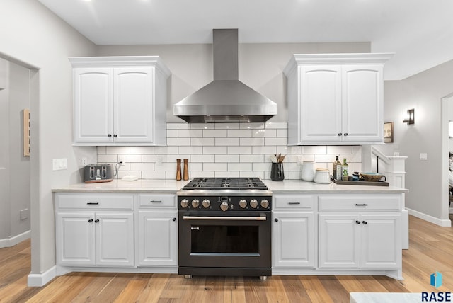 kitchen with stainless steel stove, backsplash, island range hood, and white cabinetry