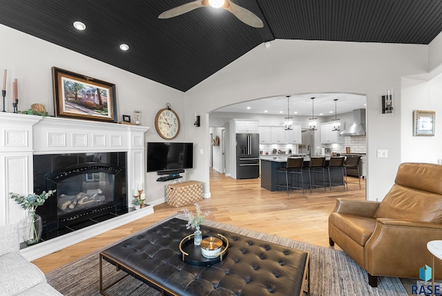 living room with a tiled fireplace, ceiling fan, light hardwood / wood-style flooring, and vaulted ceiling