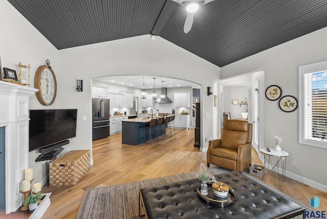 living room with light hardwood / wood-style floors, ceiling fan, lofted ceiling with beams, and sink