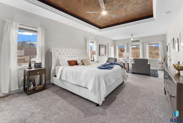 carpeted bedroom featuring ceiling fan, a tray ceiling, and multiple windows