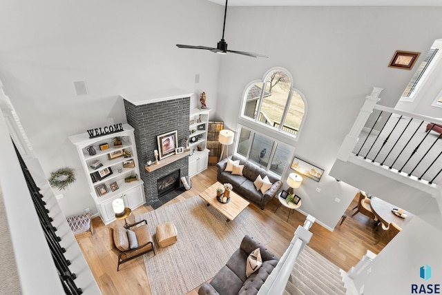 living room with a high ceiling, a fireplace, ceiling fan, and light hardwood / wood-style flooring