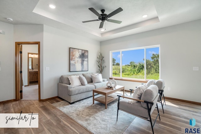 living room with wood-type flooring, a raised ceiling, and ceiling fan