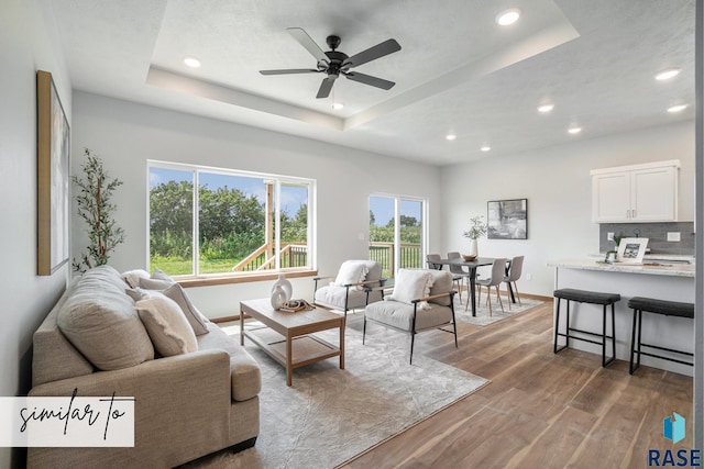 living room with ceiling fan, a tray ceiling, and hardwood / wood-style floors