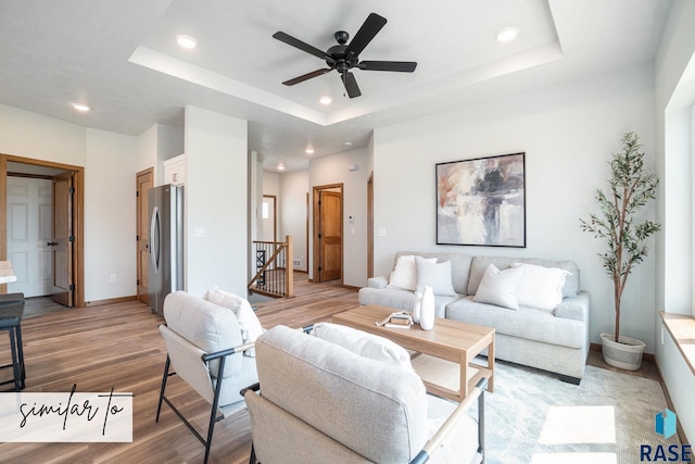 living room with ceiling fan, a tray ceiling, and light hardwood / wood-style floors