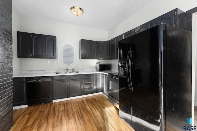 kitchen featuring light wood-type flooring, black appliances, a textured ceiling, and sink