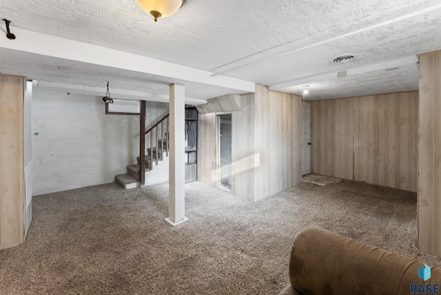 basement with a textured ceiling, wooden walls, and carpet