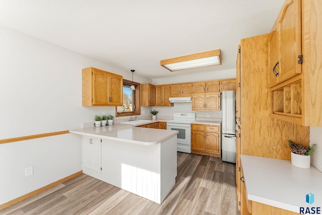 kitchen with under cabinet range hood, a peninsula, electric stove, light countertops, and freestanding refrigerator