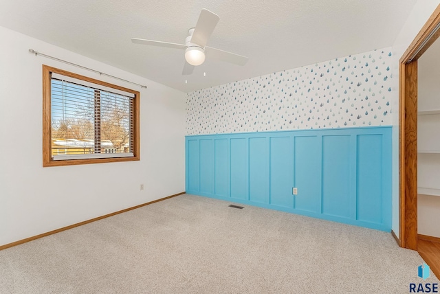 empty room with light carpet, wallpapered walls, visible vents, and wainscoting