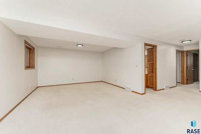 finished basement featuring light colored carpet, visible vents, a textured ceiling, and baseboards