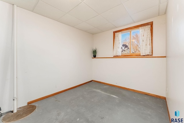 empty room featuring concrete flooring, a paneled ceiling, and baseboards