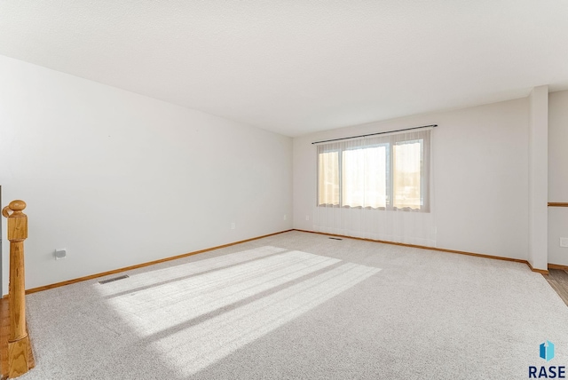 empty room with baseboards, visible vents, and light colored carpet