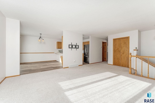 unfurnished living room with baseboards, a textured ceiling, visible vents, and light colored carpet