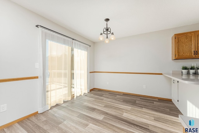 unfurnished dining area with a notable chandelier, light wood-style flooring, and baseboards