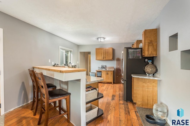 kitchen with stainless steel fridge, a breakfast bar, hardwood / wood-style floors, and kitchen peninsula