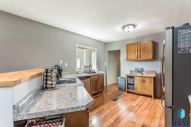 kitchen featuring kitchen peninsula, a textured ceiling, light hardwood / wood-style floors, appliances with stainless steel finishes, and sink