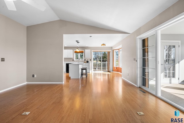 unfurnished living room with sink, light wood-type flooring, and vaulted ceiling