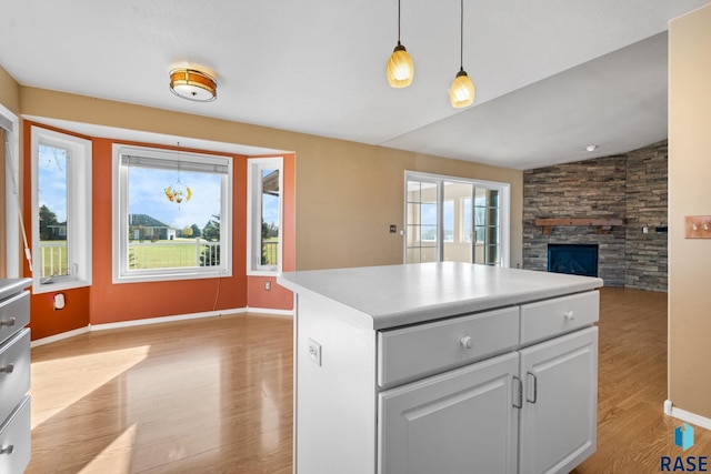 kitchen with decorative light fixtures, a center island, lofted ceiling, light hardwood / wood-style floors, and a stone fireplace