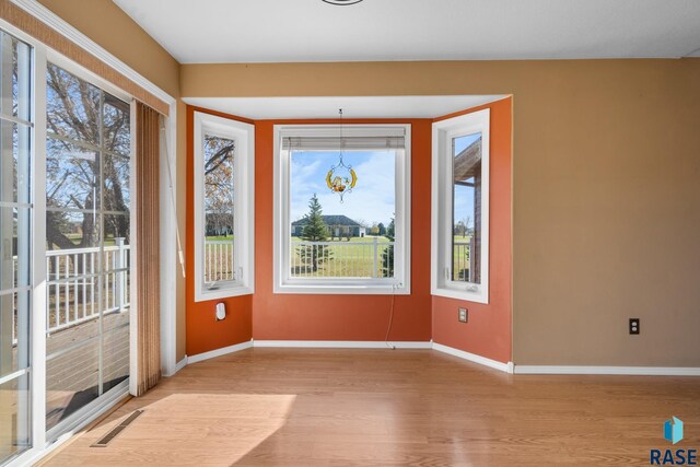 spare room with an inviting chandelier, light wood-type flooring, and plenty of natural light