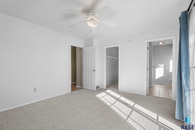 unfurnished bedroom featuring a closet, a walk in closet, ceiling fan, and light carpet