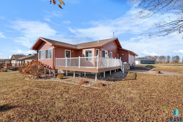 back of house with a wooden deck, an outdoor fire pit, and a lawn