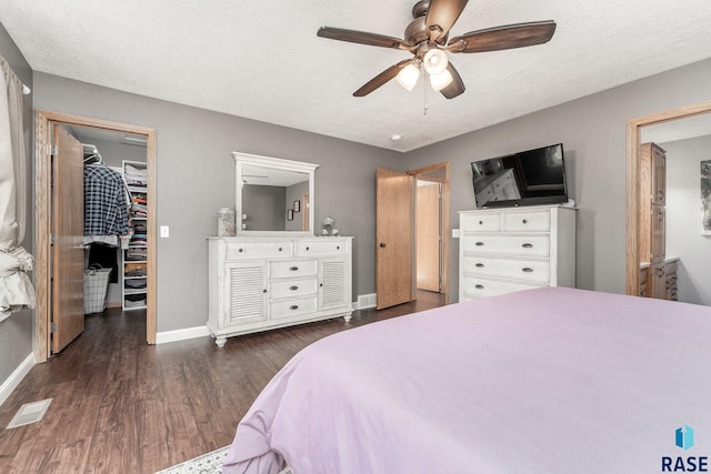 bedroom with a closet, ceiling fan, dark wood-type flooring, a textured ceiling, and a walk in closet