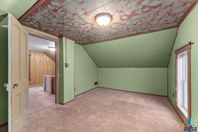 bonus room featuring lofted ceiling, wooden walls, and light colored carpet