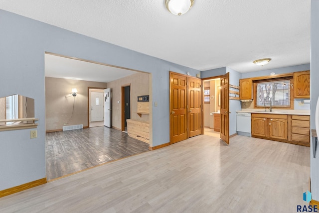 kitchen with sink, white dishwasher, a textured ceiling, and light hardwood / wood-style flooring