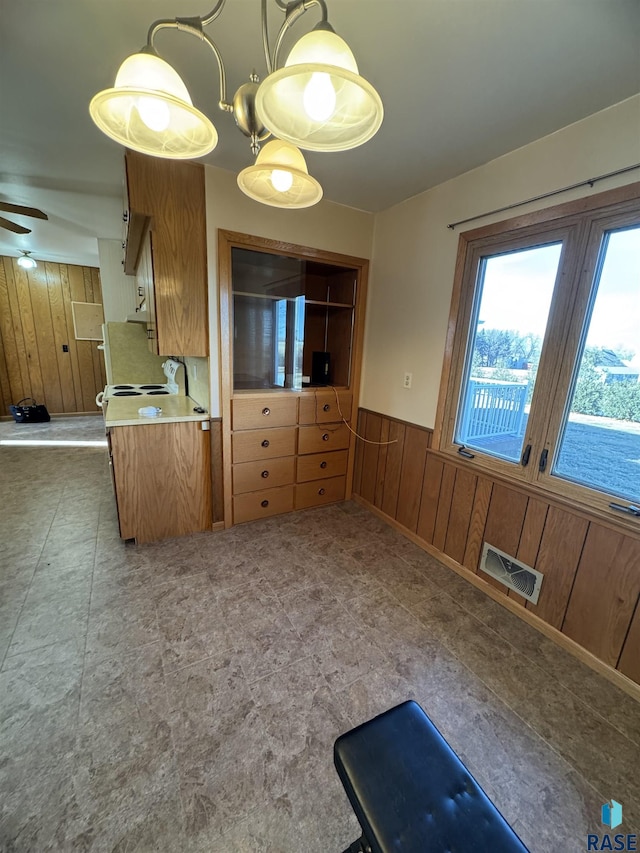 kitchen featuring ceiling fan, decorative light fixtures, and wood walls