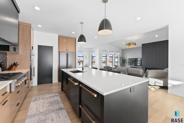 kitchen with sink, decorative light fixtures, lofted ceiling, stainless steel gas stovetop, and a kitchen island with sink