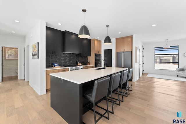 kitchen featuring wall chimney exhaust hood, tasteful backsplash, stove, a center island with sink, and pendant lighting