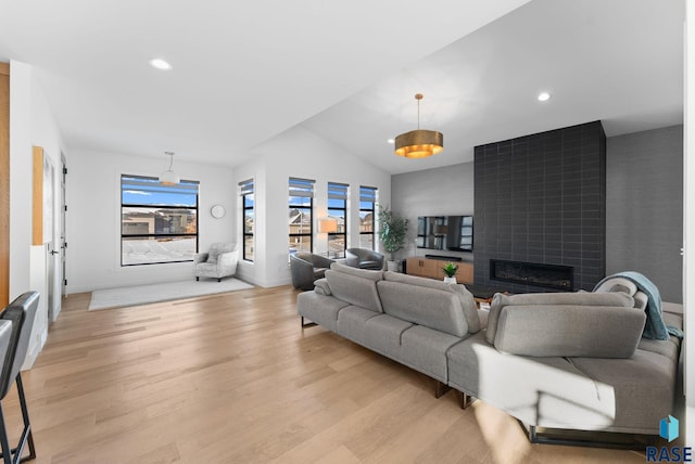 living room featuring light wood-type flooring, a tile fireplace, and vaulted ceiling